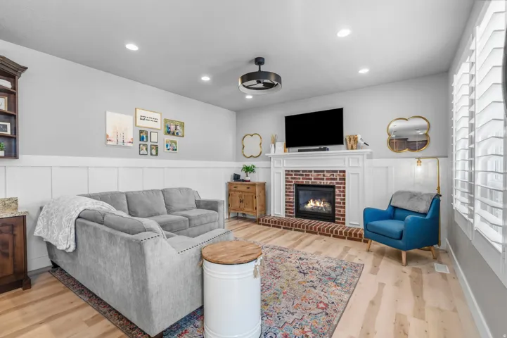 Hardwood-finish flooring, brick-surround fireplace with white mantel, recessed lighting, and white wainscoting