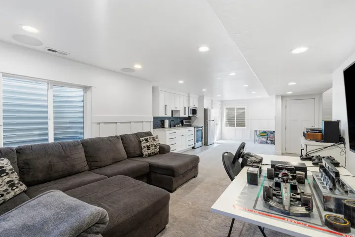 Recessed lighting illuminates the open-concept space featuring a full kitchen with white cabinetry and stainless steel appliances, a sliding glass door, and wainscoting details