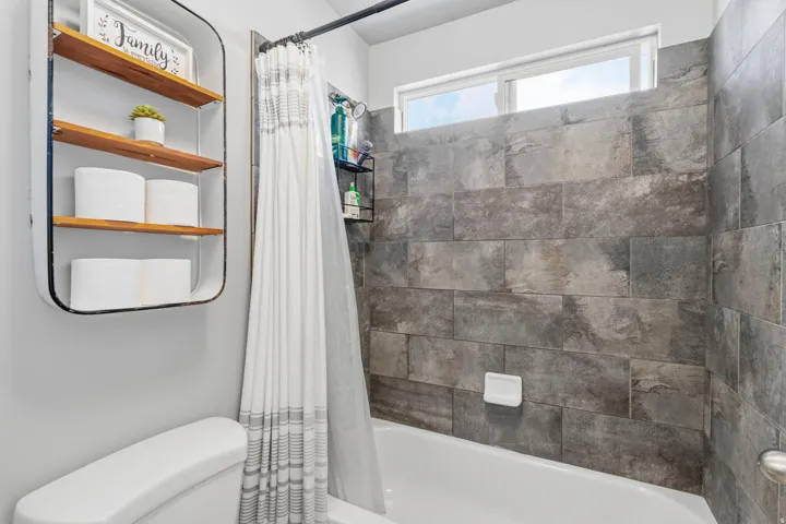 Full-height tiled shower surround, white bathtub, and transom window