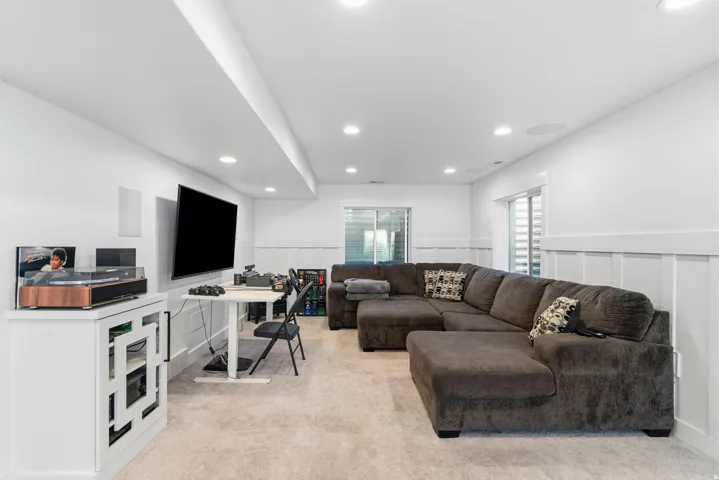 Recessed lighting, wall-mounted television, board and batten wall detailing, light-colored carpeting, and sliding glass doors
