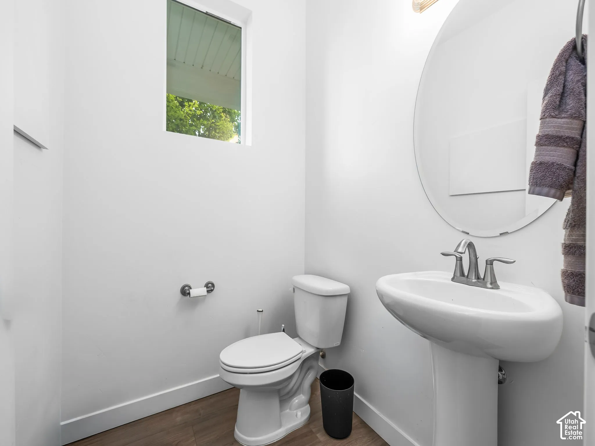 Pedestal sink with a chrome faucet, oval wall-mounted mirror, and wood-finish flooring