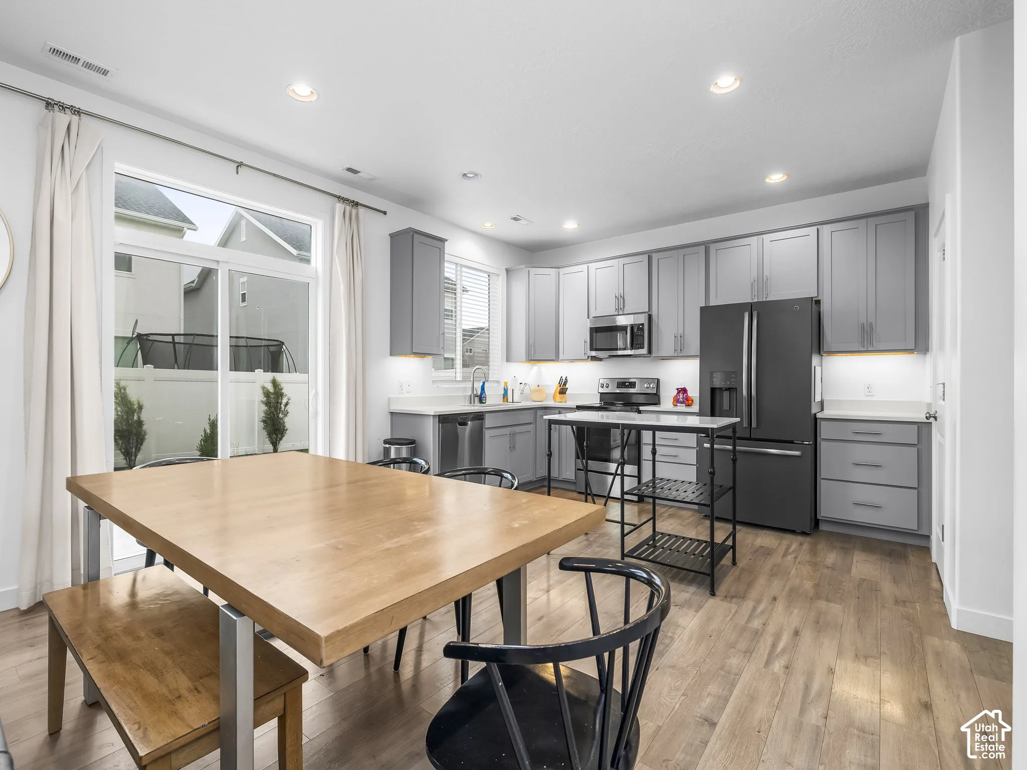 Modern kitchen with gray cabinetry, stainless steel appliances, wood-finish flooring, recessed lighting, and sliding glass doors