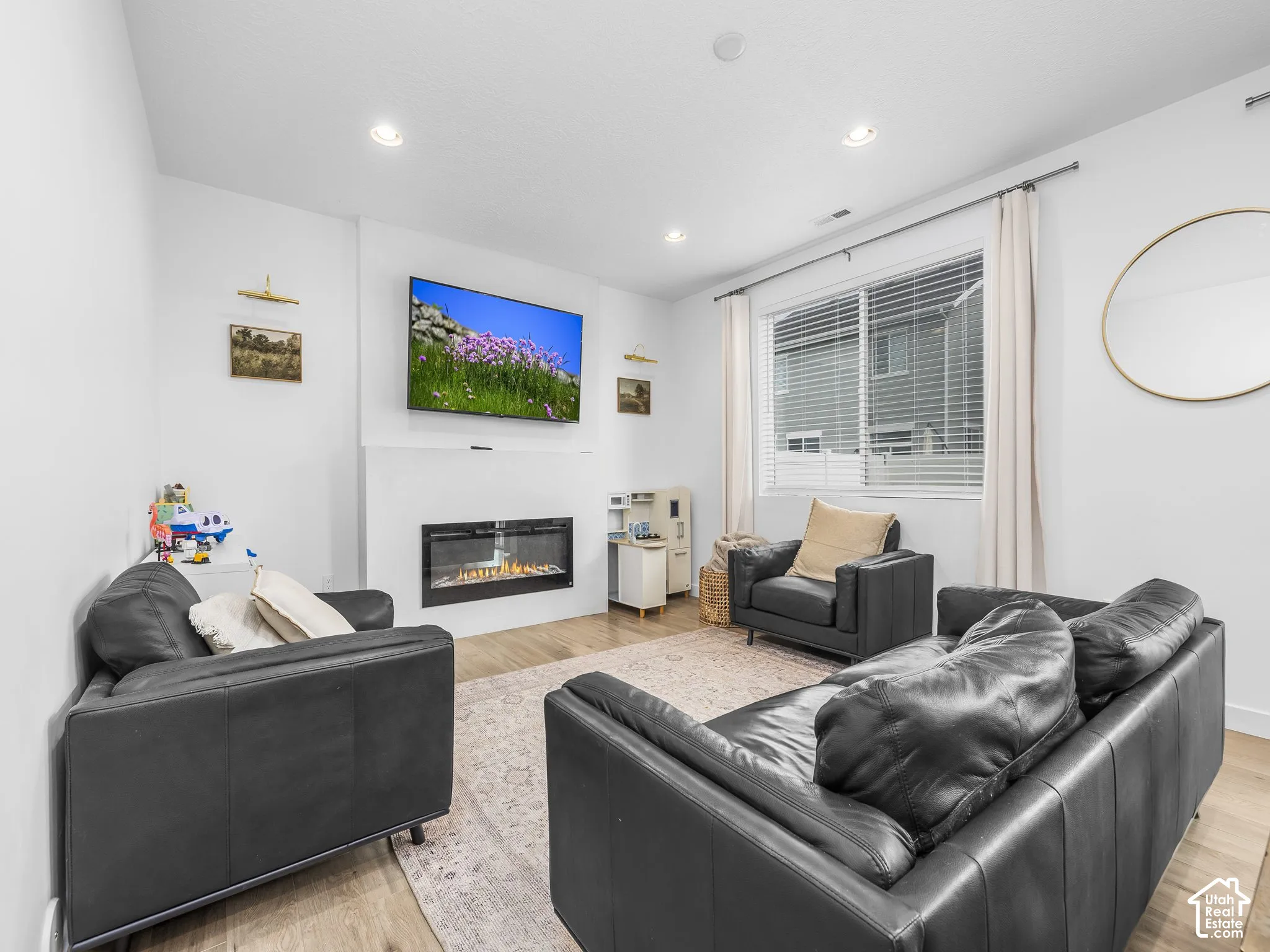 Recessed lighting, wood-finish flooring, a linear electric fireplace, and a large window with blinds and drapes