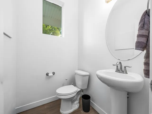 Pedestal sink with a chrome faucet, oval wall-mounted mirror, and wood-finish flooring