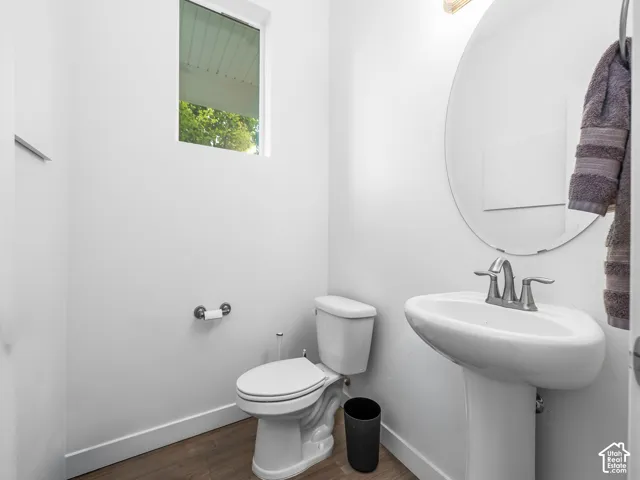 Pedestal sink with a chrome faucet, oval wall-mounted mirror, and wood-finish flooring