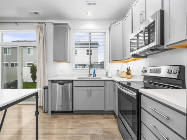 Kitchen featuring light gray cabinetry, stainless steel appliances, light-toned countertops, wood-finish flooring, and a sliding glass door