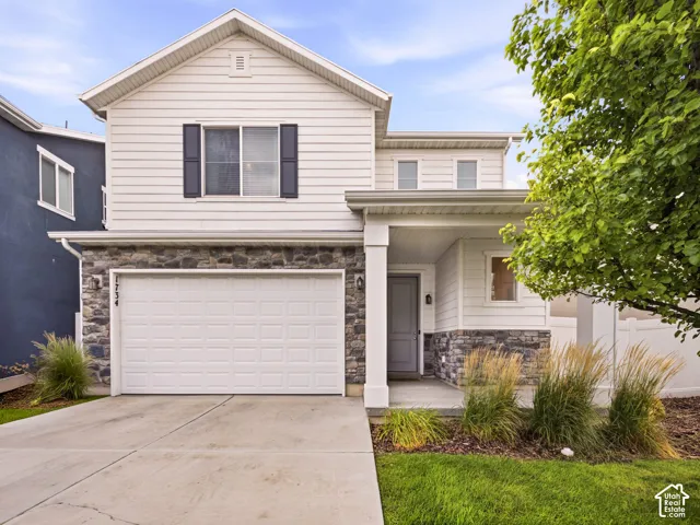 Two-story residence featuring a stone and siding exterior, an attached garage, a covered entry, and a concrete driveway