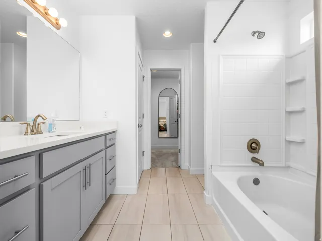 Vanity with gray cabinetry, white countertop, and brushed brass fixtures