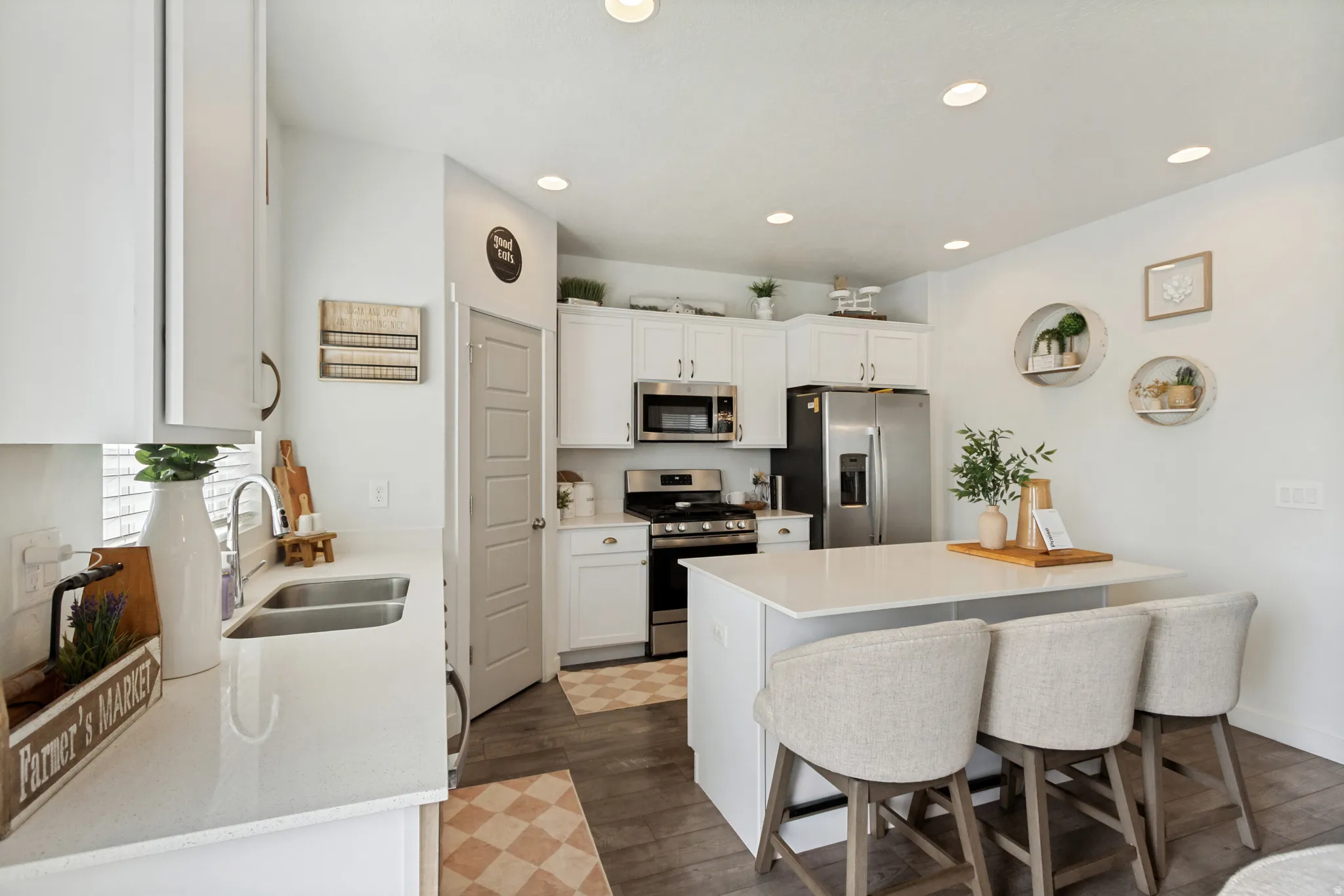 White cabinetry with brushed nickel hardware, stainless steel appliances, dual basin sink, central island, and wood-finish flooring