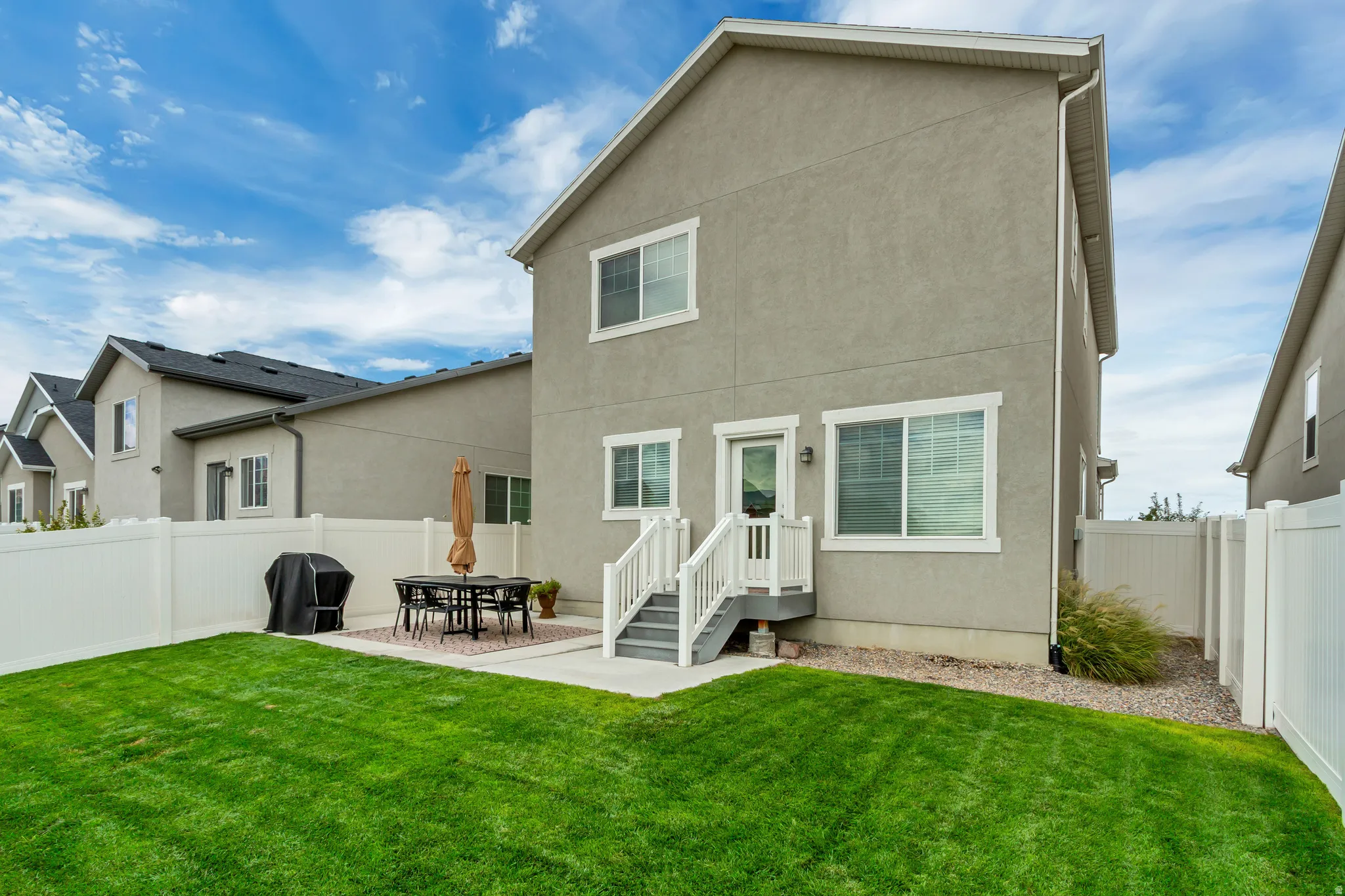 Spacious backyard oasis featuring a manicured lawn, composite deck with dining area, white vinyl fencing, and direct access from the home's sliding glass doors