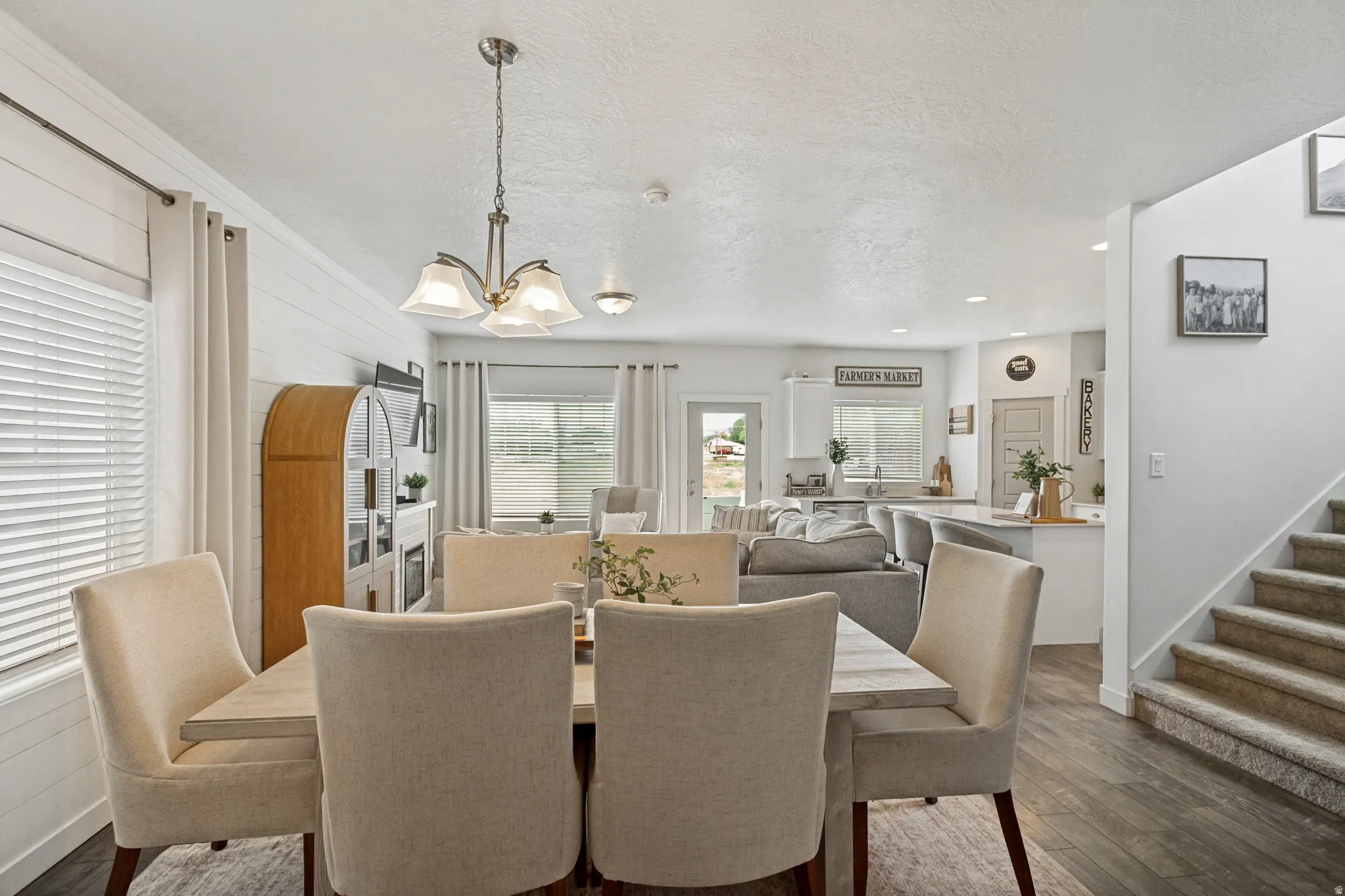 Open-concept living space with dark wood-finish flooring, white shiplap accent wall, and a multi-tiered chandelier