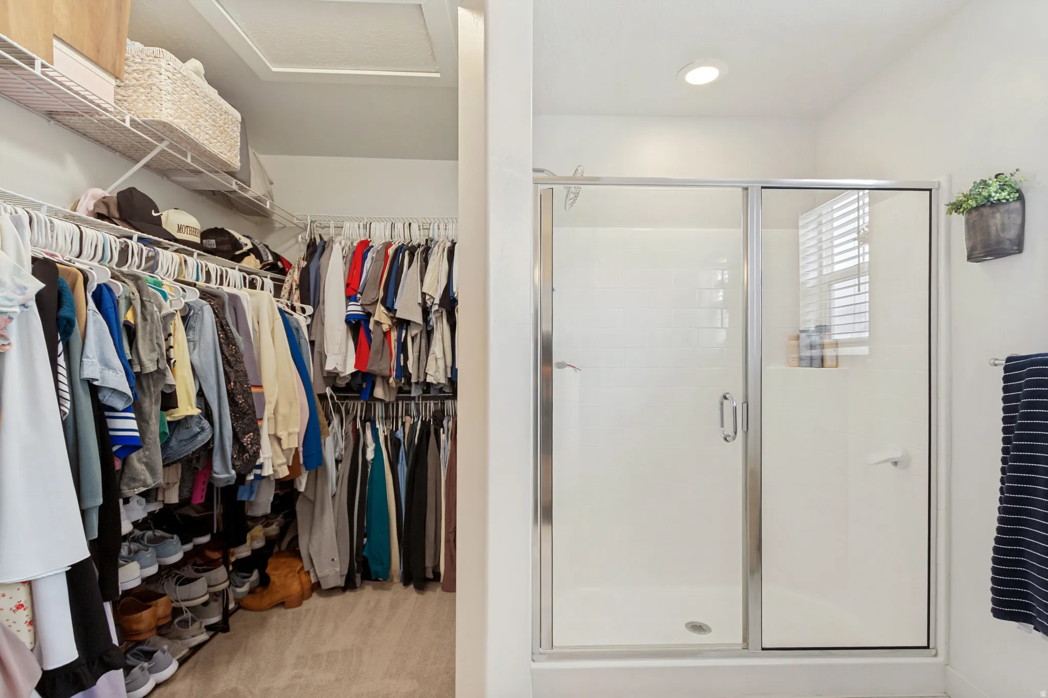 Primary Walk-In Closet with extensive rod-and-rail storage system, wood-finish flooring, built-in shelving with woven storage baskets, and abundant natural light from transom window