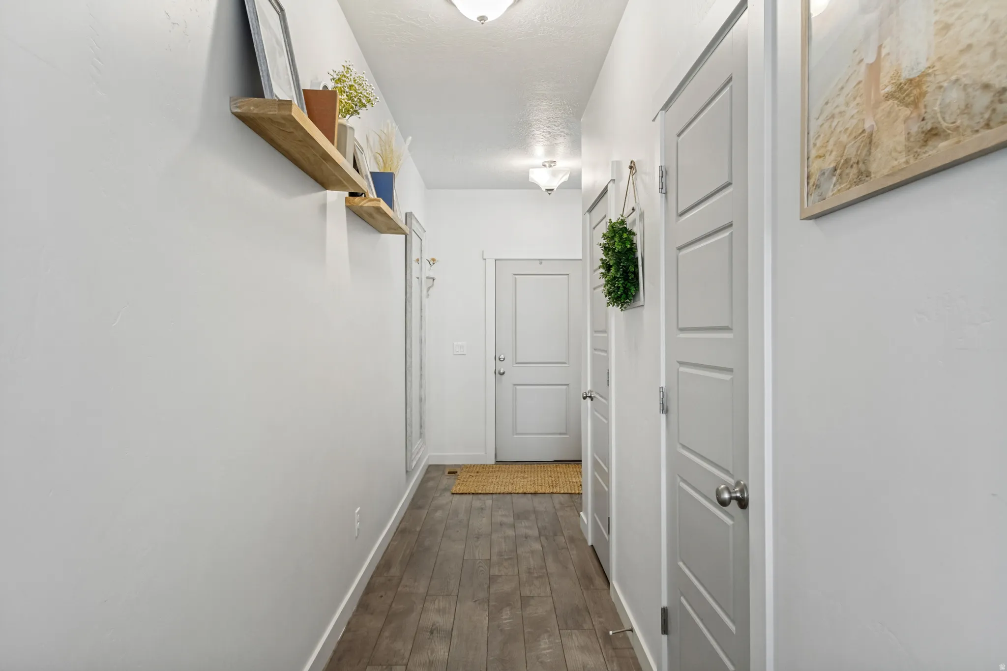 Bright hallway featuring wood-finish flooring, white six-panel doors, floating wooden shelving, and recessed ceiling lighting throughout