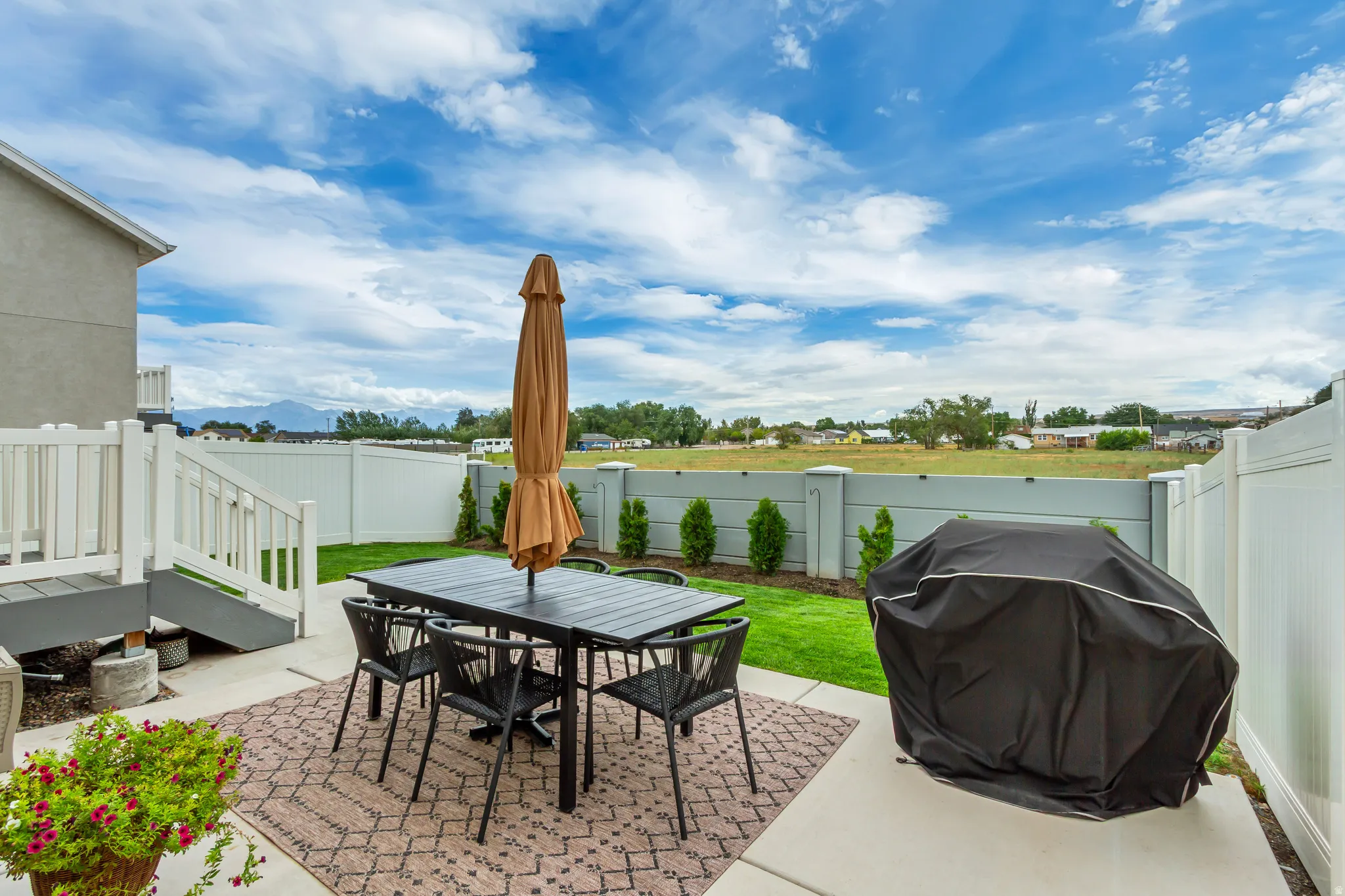 Paved patio area, raised deck with white railings, manicured lawn, and privacy fencing