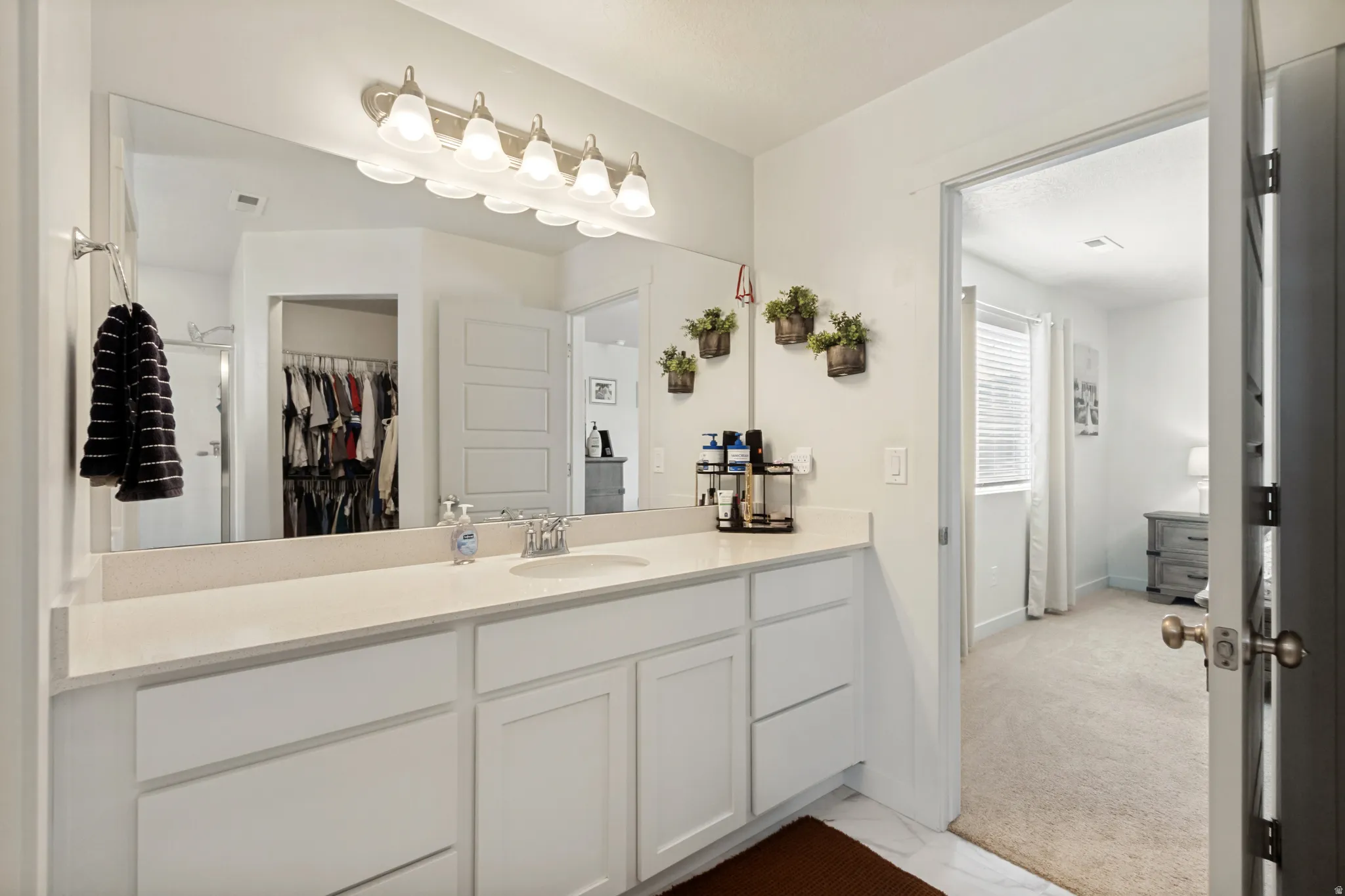 White vanity with ample storage, integrated single-basin sink, large wall-mounted mirror, and overhead light fixture