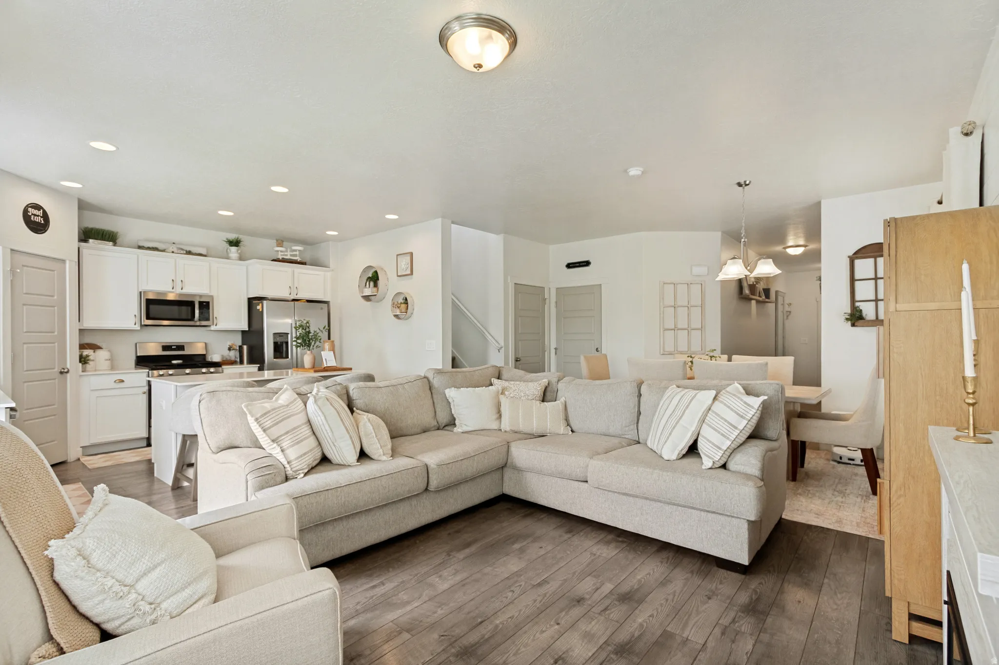 Open-concept living space featuring wood-finish flooring, recessed lighting, white cabinetry, stainless steel appliances, and a kitchen island with seating