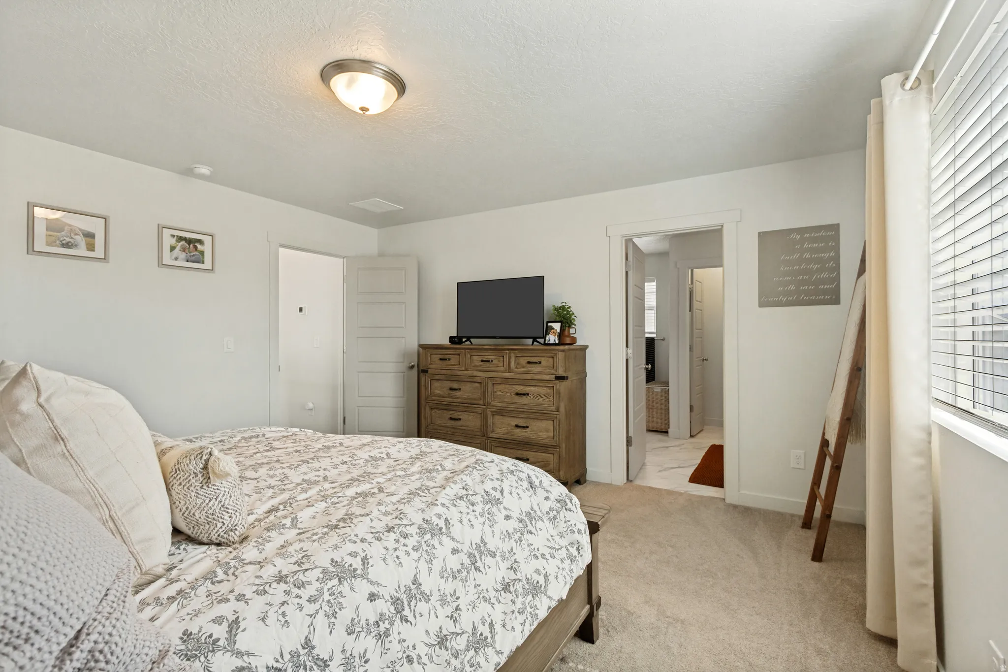 Plush carpet flooring, neutral wall tones, window with horizontal blinds, and a permanent ceiling light fixture