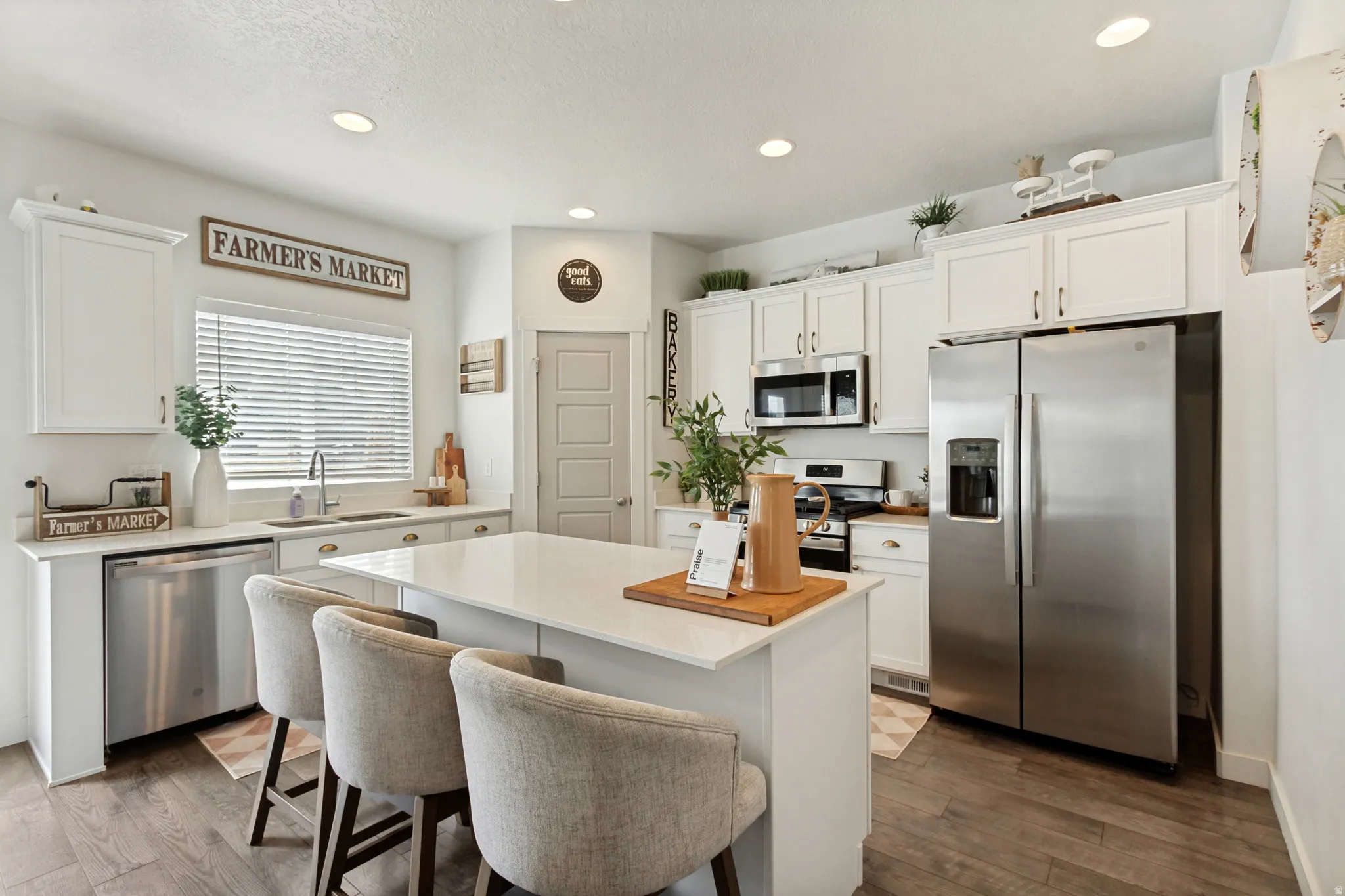 Kitchen featuring white shaker cabinetry, stainless steel appliances, a center island with countertop seating, and wood-finish flooring