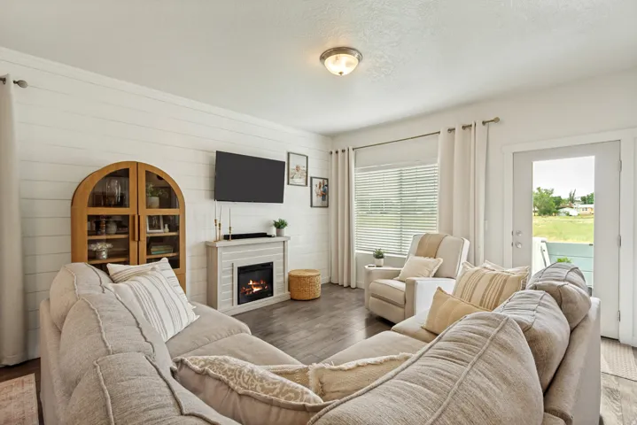 Shiplap accent wall, wood-finish flooring, electric fireplace, ceiling-mounted light fixture, and white door with exterior access