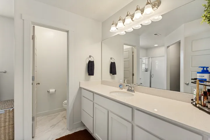 Long vanity with an integrated sink, broad wall-mounted mirror, and overhead lighting fixture