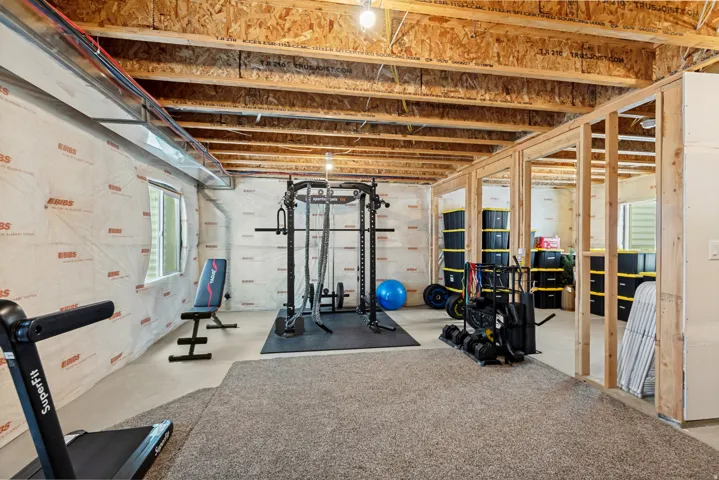 Unfinished basement with exposed ceiling joists, framed interior walls, and a window for natural light