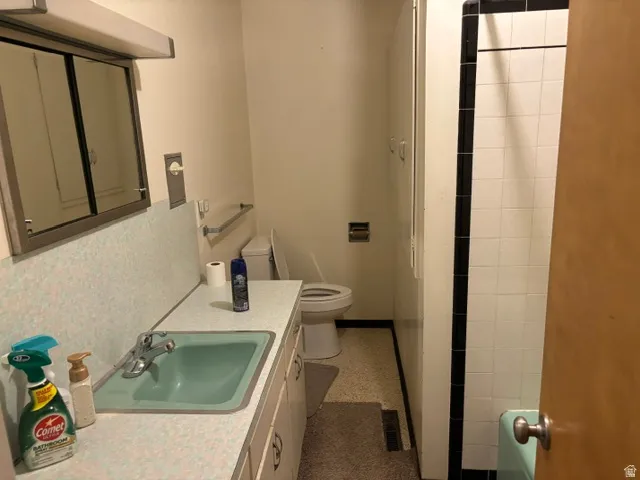 Vanity with integrated sink, wall-mounted medicine cabinet, toilet, and tiled shower surround