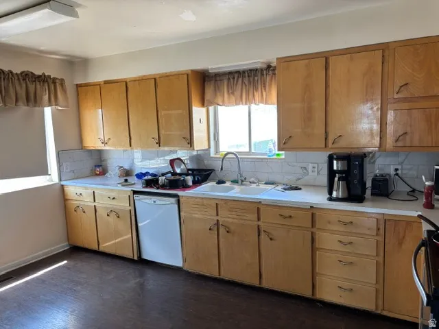 Wood-finish cabinetry, white countertops, tile backsplash, stainless steel sink, and wood-finish flooring