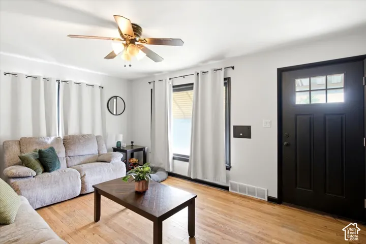 Hardwood-style flooring throughout, featuring a multi-paneled entry door with clear glass, a ceiling fan with integrated lighting, and multiple windows