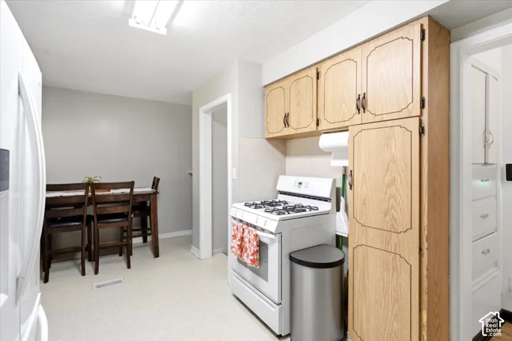 Kitchen featuring wood-finish cabinetry, white appliances, and light-toned flooring