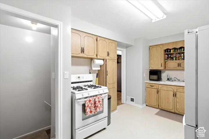 Kitchen featuring wood-finish cabinetry, a white gas range, and a drop-in sink with a white countertop