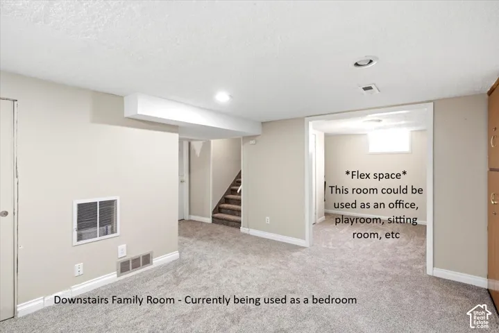Recessed lighting, light-toned carpeting, neutral wall paint, and a doorway opening to an additional room