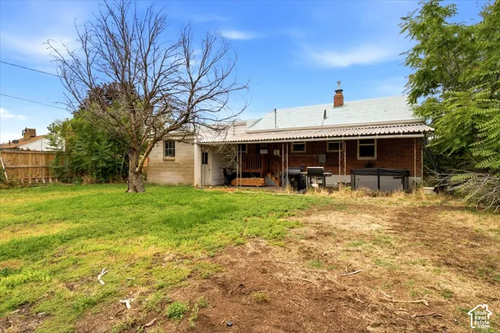 Expansive backyard featuring a partial grass lawn, mature trees, and a brick exterior with an attached covered patio