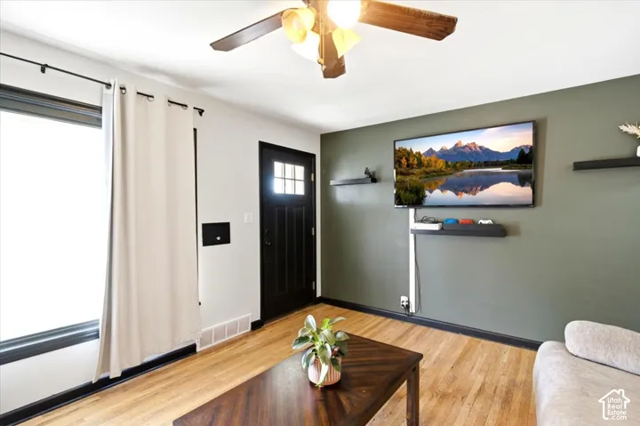 Wood-finish flooring, ceiling fan with integrated lighting, dark accent wall, and a multi-pane front door