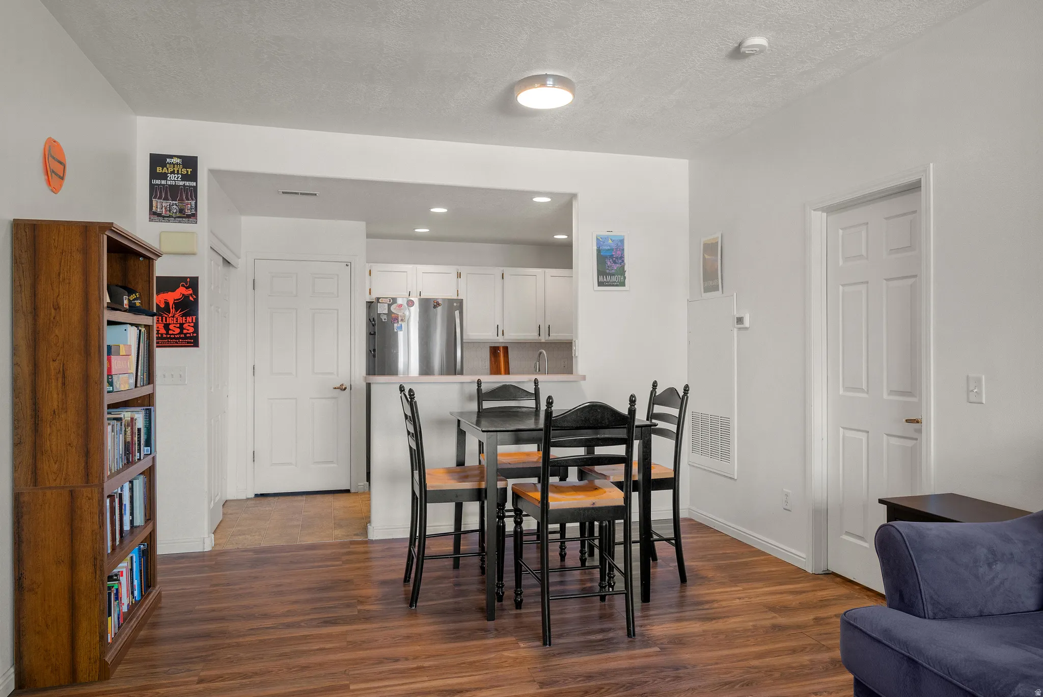 Wood-finish flooring throughout, white walls, and a recessed kitchen opening with white cabinetry