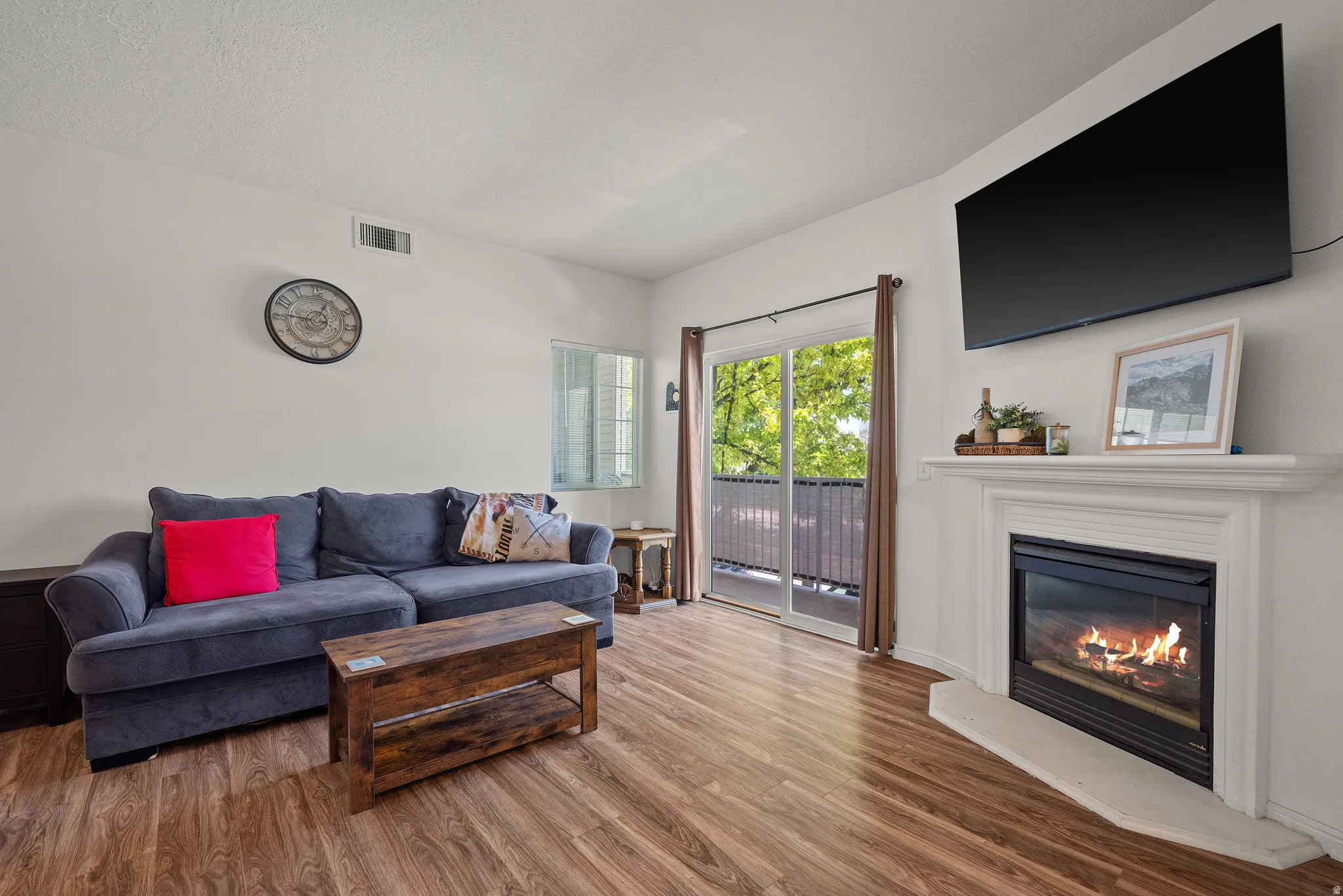 Living area featuring wood-finish flooring, a white mantel, and a fireplace with a black insert