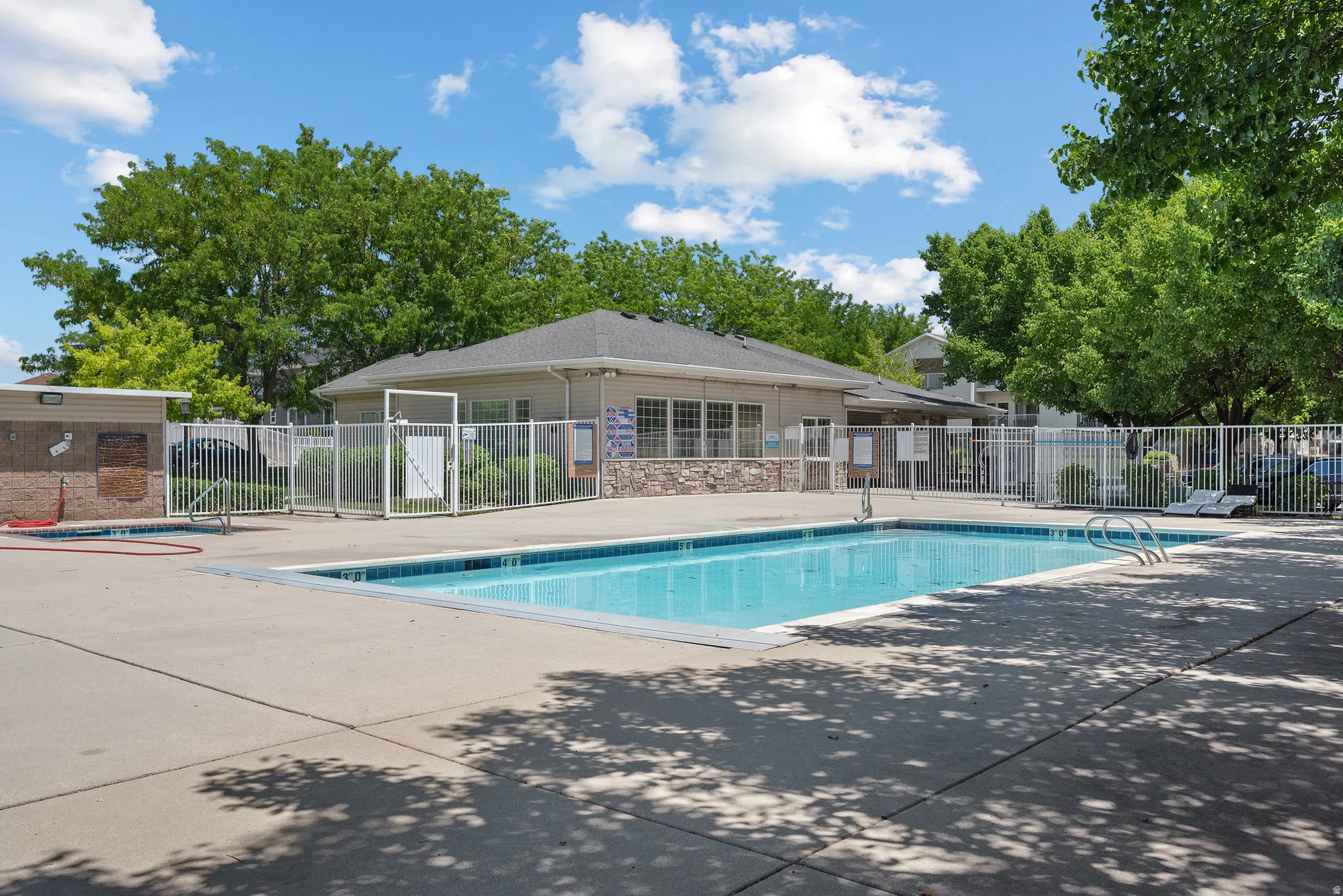 Outdoor swimming pool with concrete decking, surrounding security fence, and adjacent building with stone facade