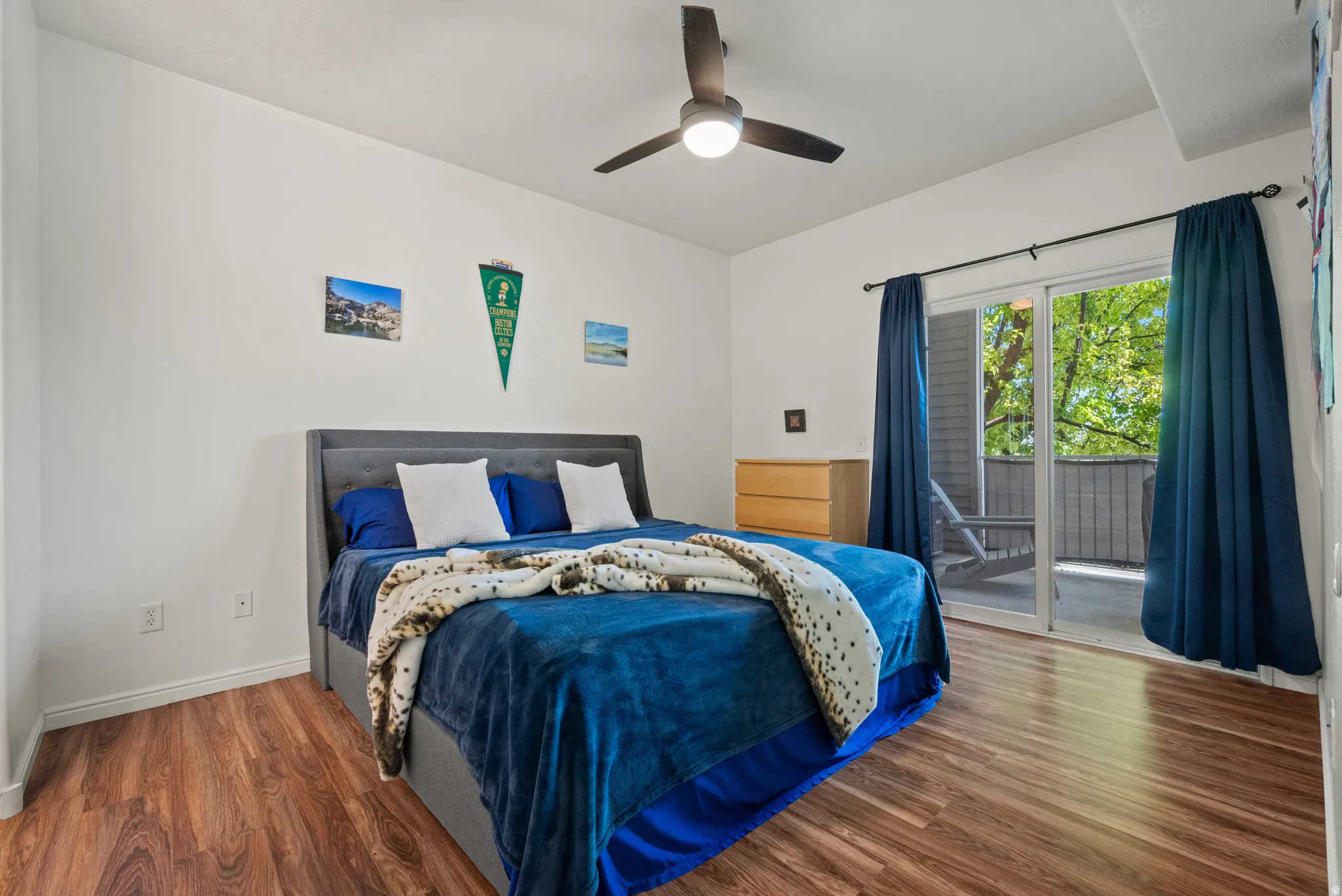Wood-finish flooring, ceiling fan with integrated lighting, white walls, and a sliding glass door leading to an outdoor balcony