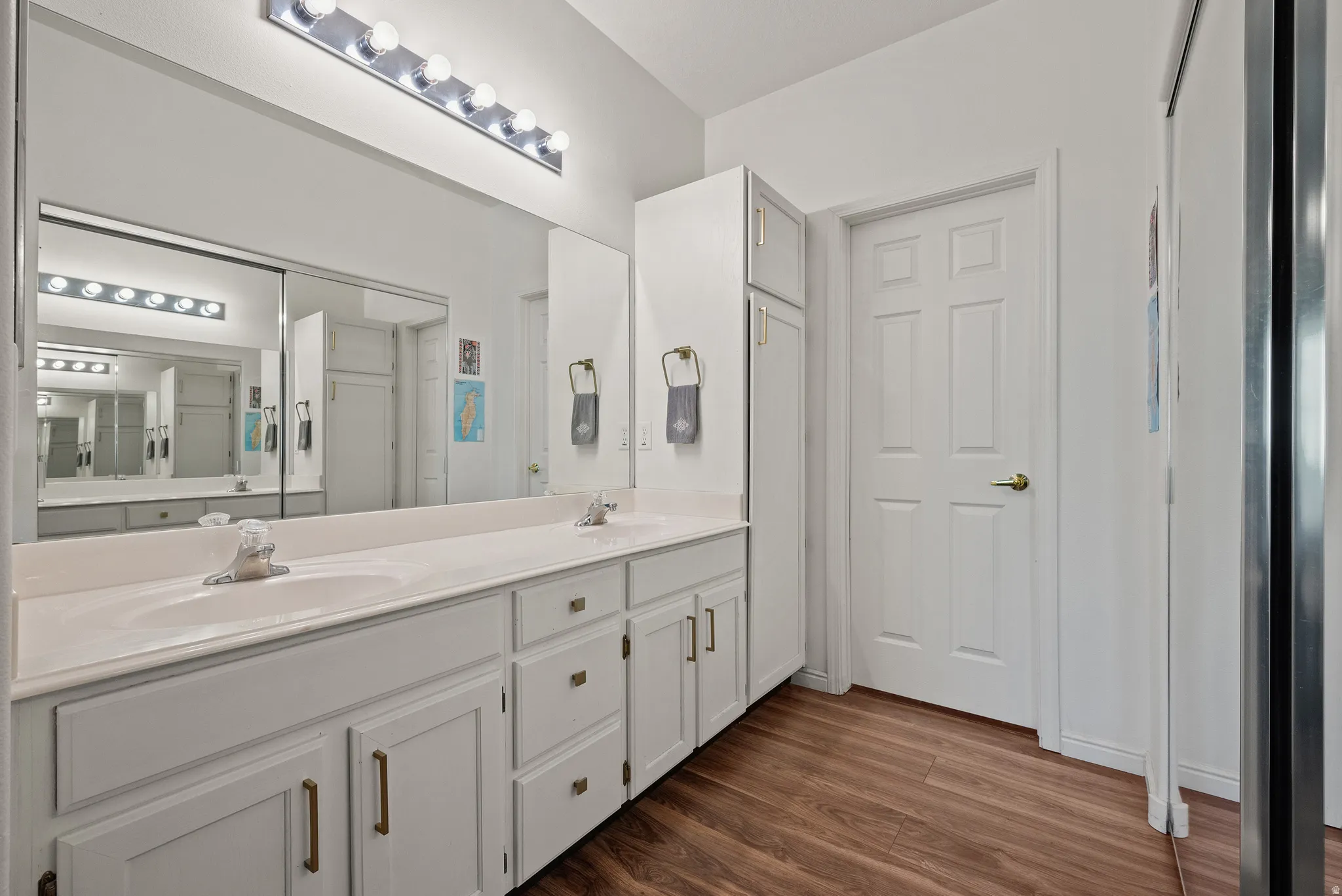 Dual vanity with undermount sinks, expansive wall-mounted mirror, wood-finish flooring, and integrated storage cabinetry