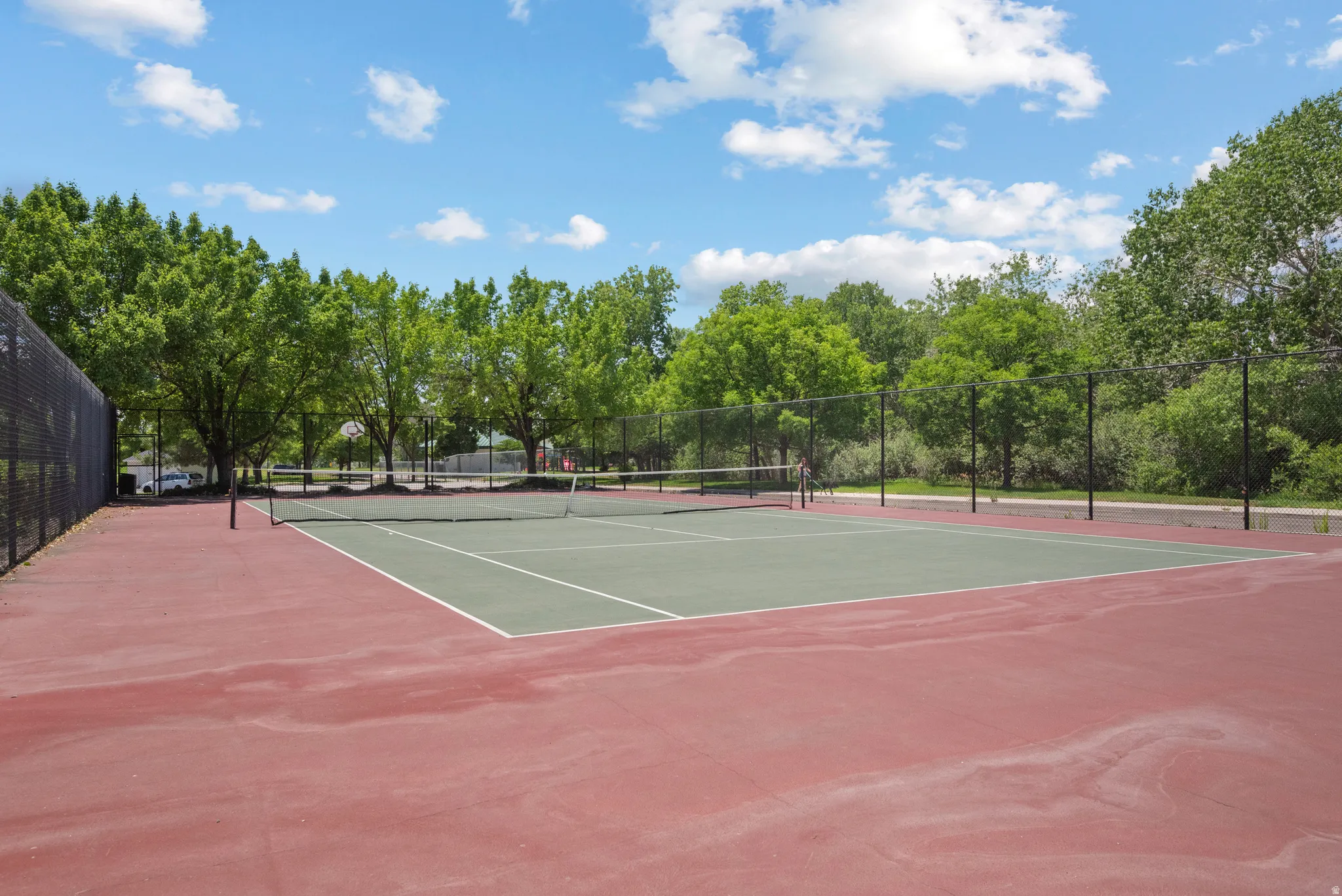 Regulation-size tennis court featuring a red hard-court surface with green playing areas and white lines