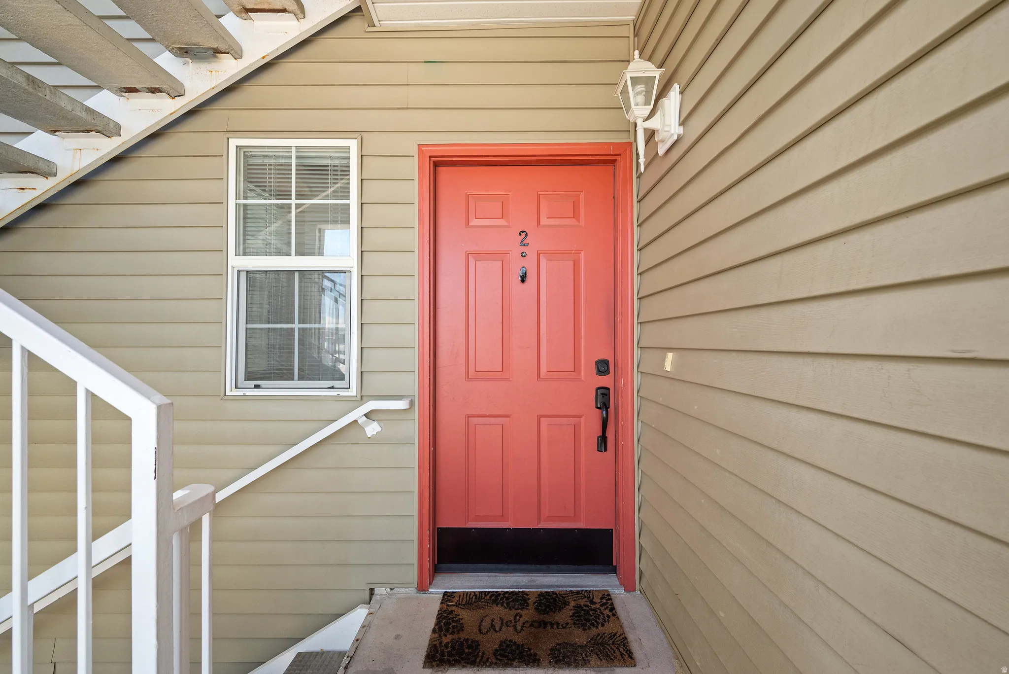 Welcoming entry featuring a bold coral-red six-panel door with satin nickel hardware, flanked by horizontal fiber-cement siding in a warm neutral tone
