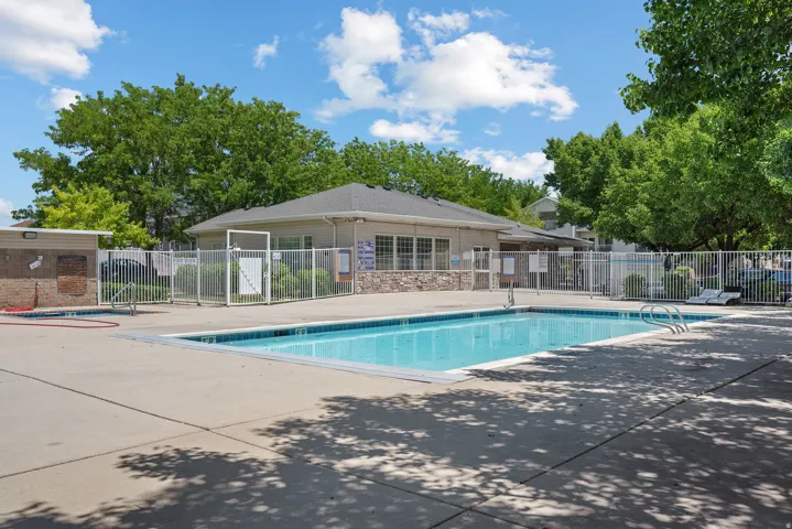 Outdoor swimming pool with concrete decking, surrounding security fence, and adjacent building with stone facade