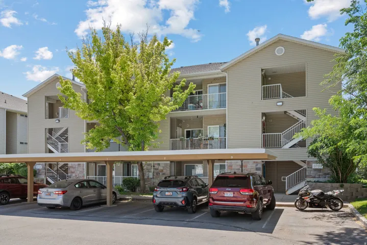Multi-story residential building with siding exterior, stone facade, covered parking structure, exterior balconies, and multiple entry points