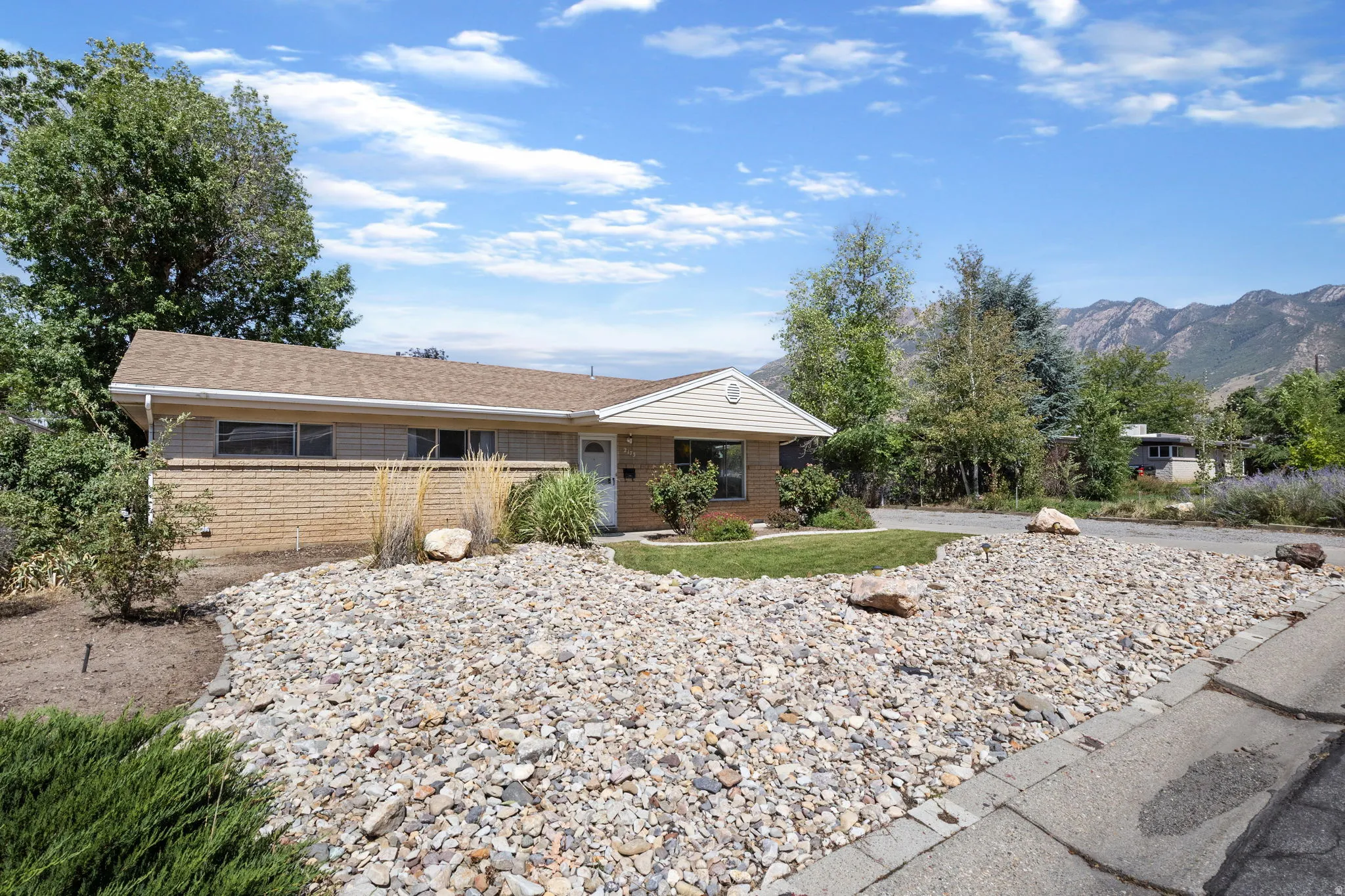 Brick and siding exterior with a pitched roof, gravel landscaping, and established trees