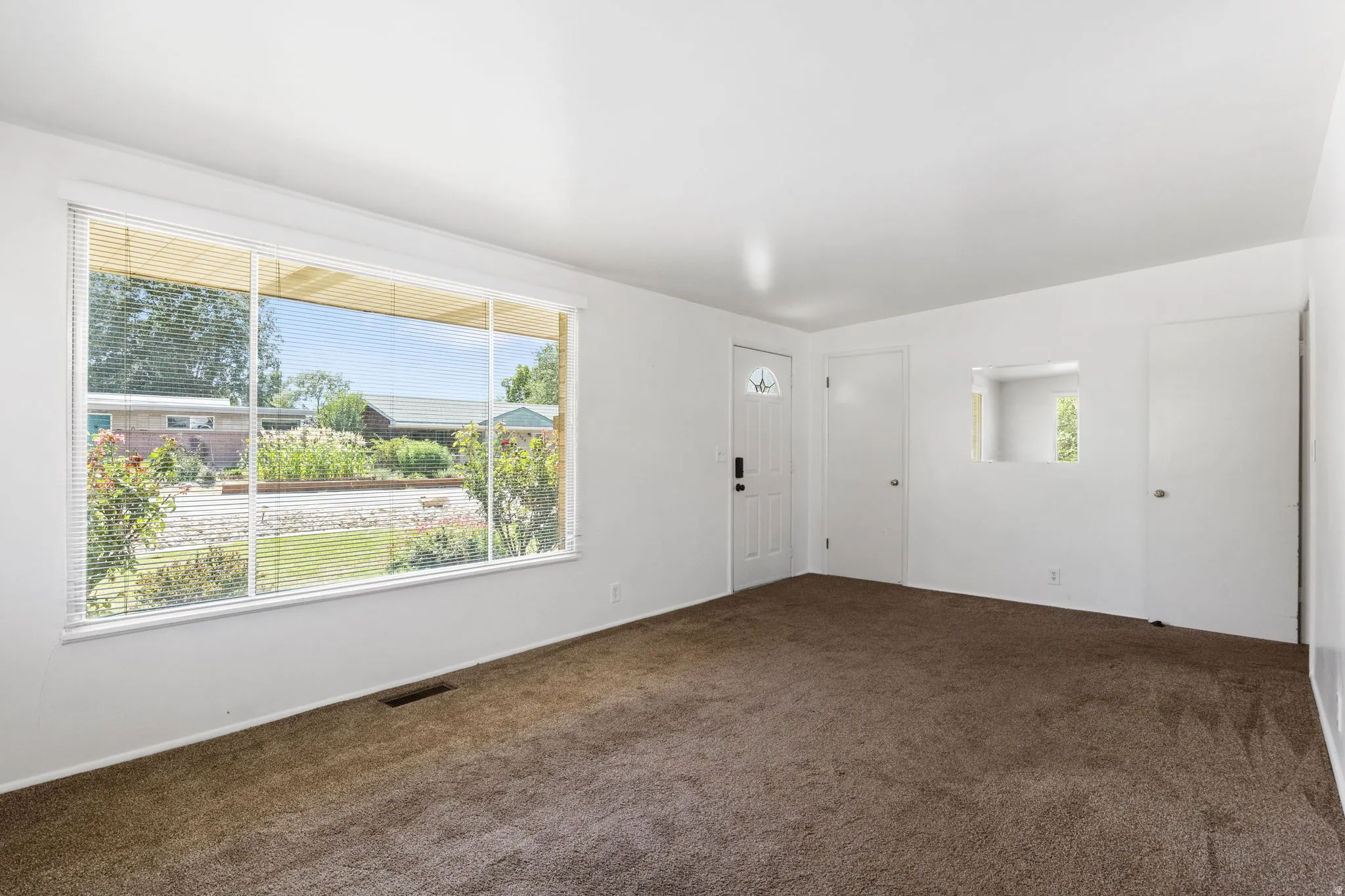 Expansive front window, white interior walls, built-in wall niche, brown carpeting, and a white entry door