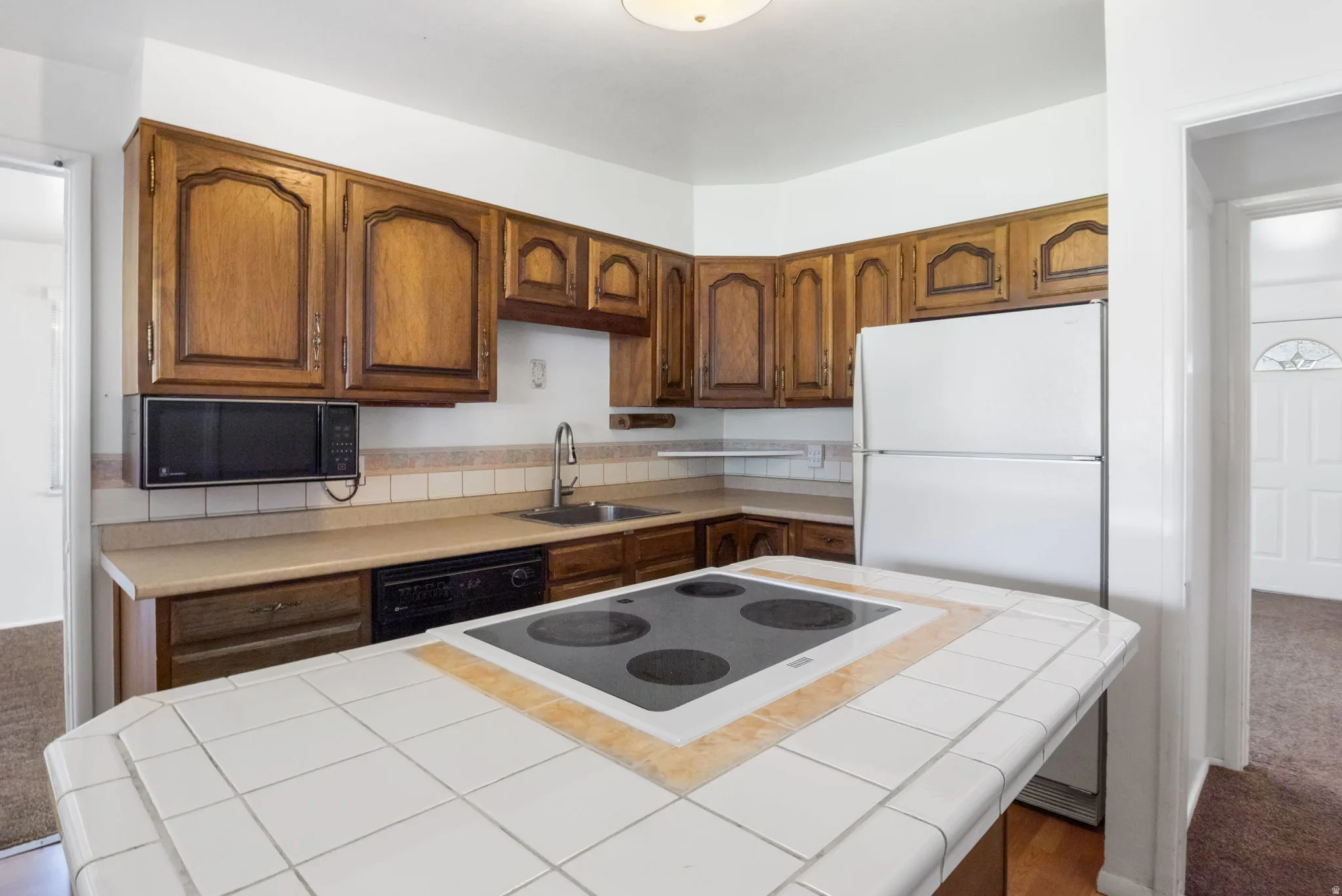 Kitchen featuring wood-finish cabinetry, tile backsplash, laminate countertops, and a tile-top island with an integrated cooktop