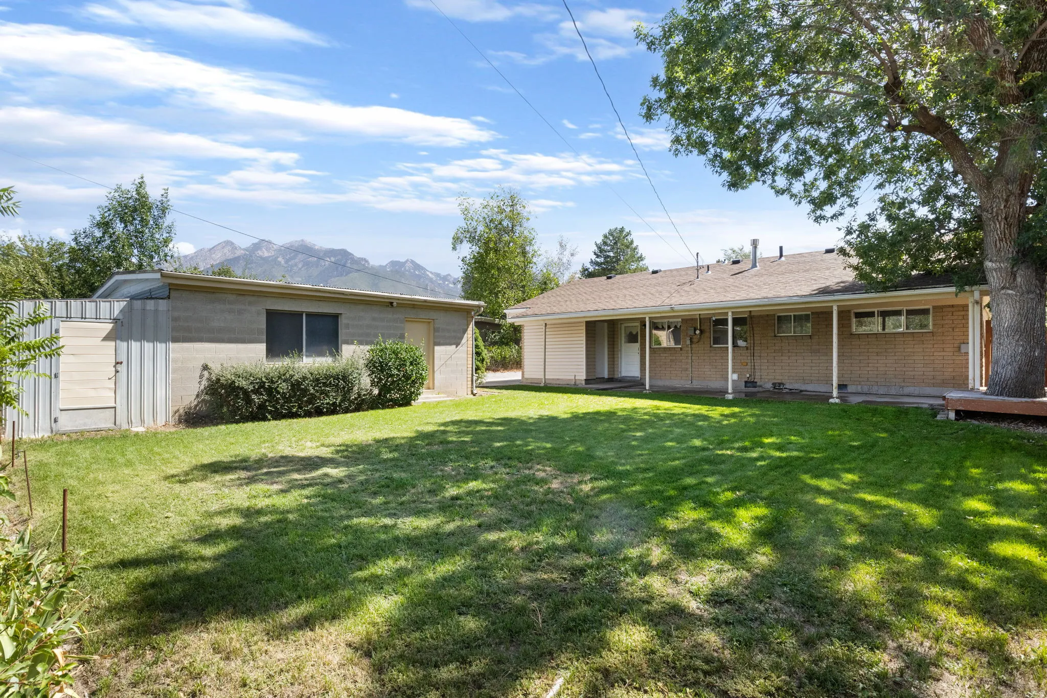 Expansive backyard with a manicured lawn, an attached covered patio, a detached auxiliary structure, and mountain scenery
