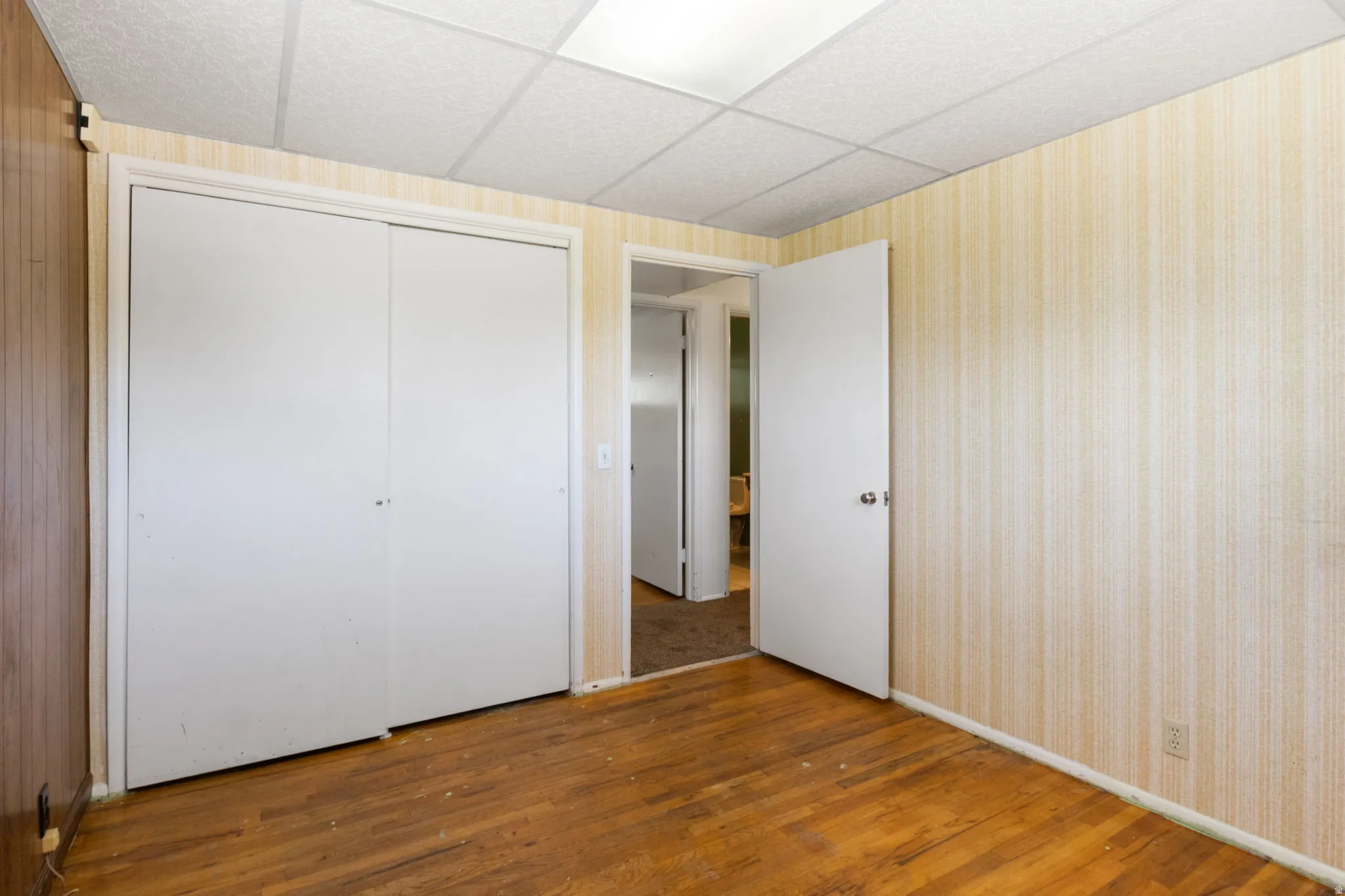 Wood-finish flooring, white bi-fold closet doors, textured wall covering, and a drop ceiling with recessed lighting