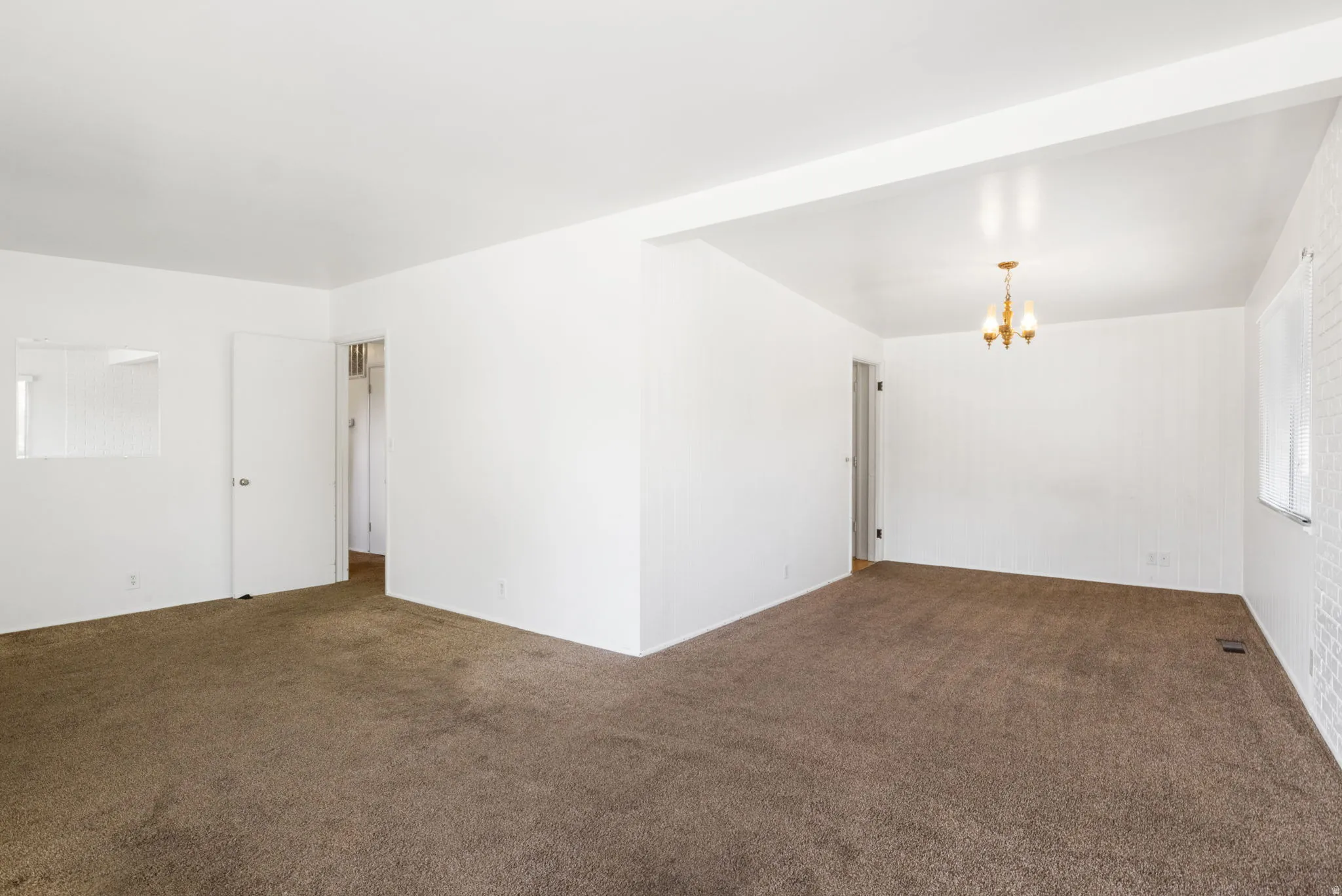 Spacious interior with neutral carpeting, white walls, and a classic chandelier