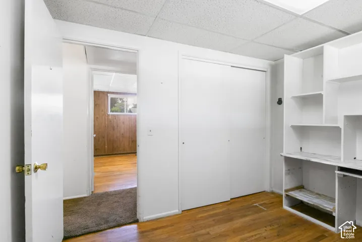 Hardwood-style flooring, white built-in shelving, white sliding closet doors, white walls, and a dropped ceiling