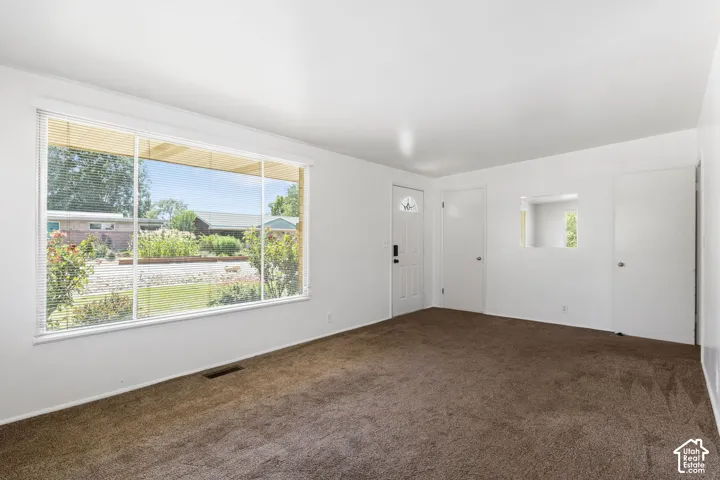 Expansive front window, white interior walls, built-in wall niche, brown carpeting, and a white entry door